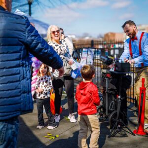 Ty twisting balloons with a line of guests at an outdoor festival.