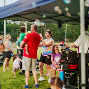 Ty twisting balloons with a line of guests at an outdoor festival.